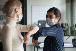 Smiling,Diverse,Female,Colleagues,Wearing,Protective,Face,Masks,Greeting,Bumping